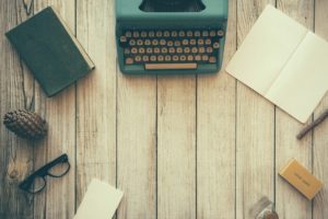 DEcorative image of a desk with a typewriter, notepads, eye glasses and pens. 